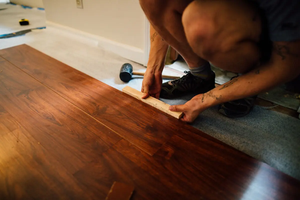 Vakman legt een houten vloer met een slagblok en rubber hamer