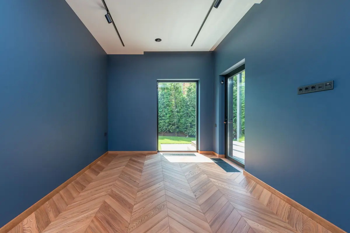 Lege moderne kamer met blauwe wanden, tuindeur en warme visgraatvloer
